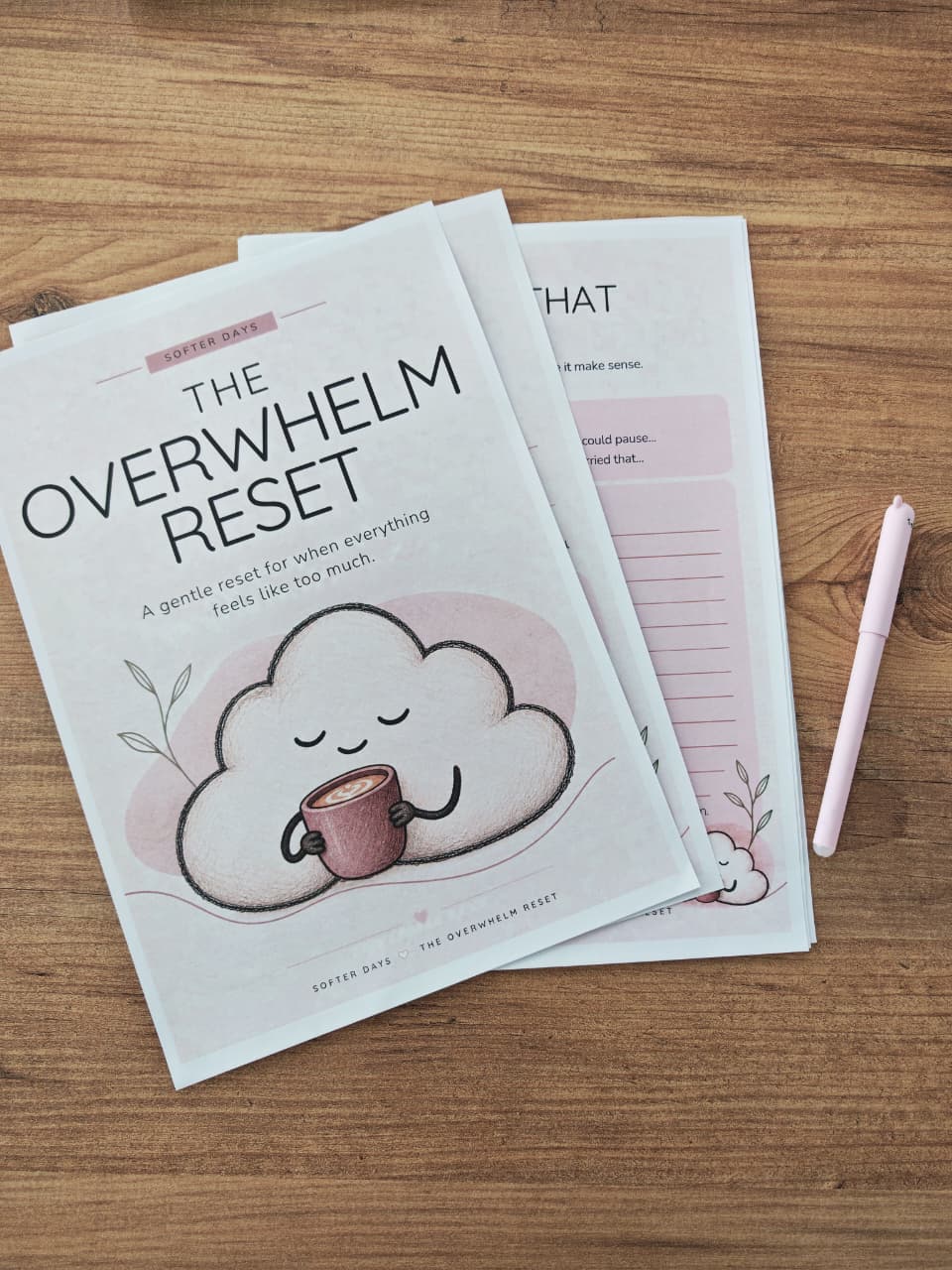 Printed pages from The Overwhelm Reset printable spread across a wooden table, with a pink pen beside the gentle cloud cover.
